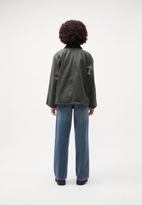 Tamsiai žalia odinė striukė su laisvu siluetu, nuleistais pečiais ir matomomis siūlėmis, derinama su šviesiai mėlynomis plačiomis kelnėmis ir juodais batais.