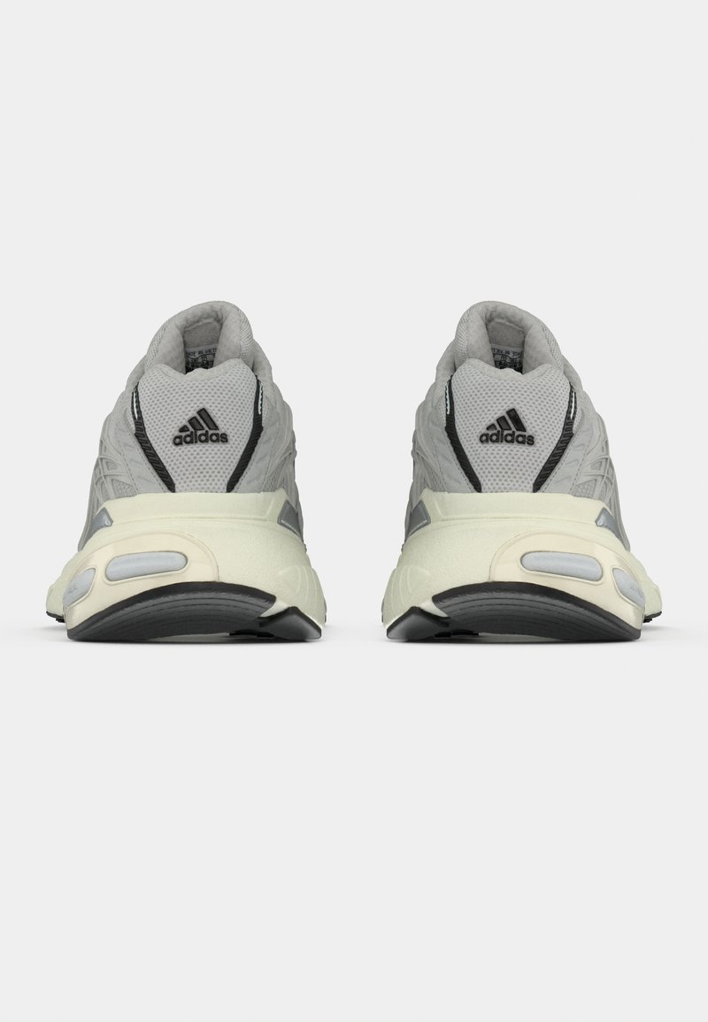 Sneaker in tessuto grigio con parte superiore in rete testurizzata, accenti neri e suola crema. Presenta un tallone imbottito e dettagli riflettenti.