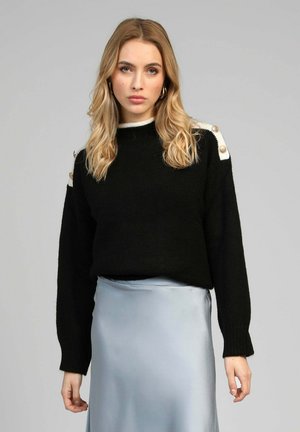 Pull noir en maille avec manches longues, orné de boutons décoratifs sur des accents blancs aux épaules, associé à une jupe en satin bleu clair.