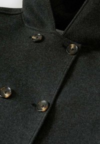 Mörkgrå ullrock med dubbelknäppt front som har fyra knappar i bruna nyanser och en hög krage.