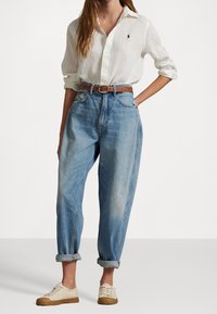 Bílé lněné košile s knoflíky, světle modré volné džínové kalhoty s ohrnutými manžetami, hnědý kožený opasek a béžové plátěné boty s gumičkovými podrážkami.