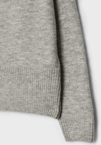 Pull en tricot gris avec une manchette côtelée et un tissu doux et texturé. Le design présente peu de détails pour un profil épuré.