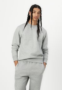 Grå genser og matchende joggebukser laget av mykt stoff, med ribbestrikkede mansjetter og en liten logo på brystet.