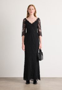 Robe longue en dentelle noire avec des manches trois-quarts, un décolleté en V et un corsage ajusté ; texture en dentelle florale transparente avec un ourlet évasé.