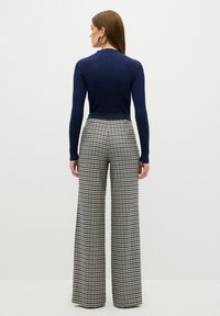 Námořnická pruhovaná top s dlouhým rukávem, doplněná o široké kalhoty s černobílým vzorem houndstooth. Hladká textura a těsně přiléhající pas.