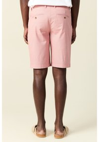 Vaaleanpunaiset shortsit, jotka on valmistettu kudotusta kankaasta. Shortsien selkäpuolella on kaksi taskua, joissa on nappikiinnitys, ja ne ovat suoran lahkeen muotoiset. Asusteena vaaleat sandaalit.