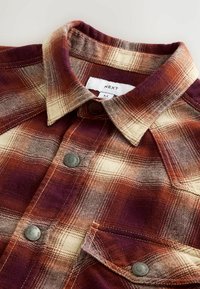 Collared red and cream plaid shirt with metal snap buttons and a front chest pocket, showing brand label "NEXT" inside the collar.