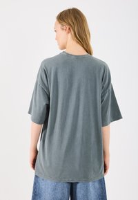 Przytulny, oversized t-shirt w zielono-szarym odcieniu z krótkimi rękawami i okrągłym dekoltem. Prosty design z nieco luźnym krojem i minimalną ilością szwów.