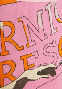 Tissu tricoté présentant du texte audacieux en orange et noir sur un fond rose, avec une illustration stylisée d'une main blanche et noire.