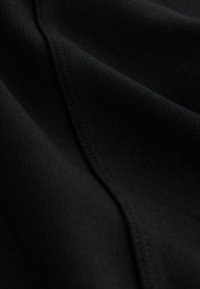 Close-up of black fabric with fine ribbed texture and visible seam running diagonally across the surface.