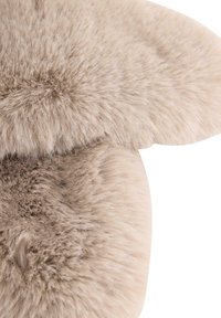 Jasno beżowy dywan z sztucznego futra o puszystej, miękkiej fakturze. Posiada zaokrąglone krawędzie oraz różne długości futra, co nadaje mu warstwowy wygląd.