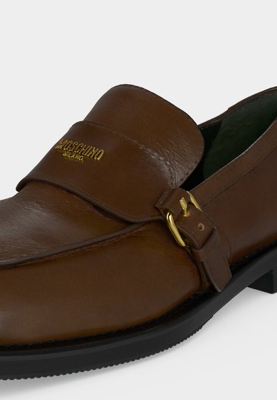 Mocassin en cuir marron avec logo Moschino Milano doré et détail de boucle dorée sur le côté et semelle noire.