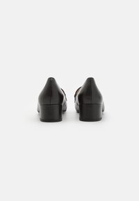 Talons en cuir noir avec un bout carré et un talon bloc discret. La texture lisse, le design minimal et les lignes épurées caractérisent la construction.