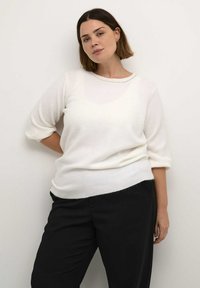 White, knitted sweater with a round neckline and three-quarter sleeves, featuring a soft texture and a relaxed fit, paired with black pants.