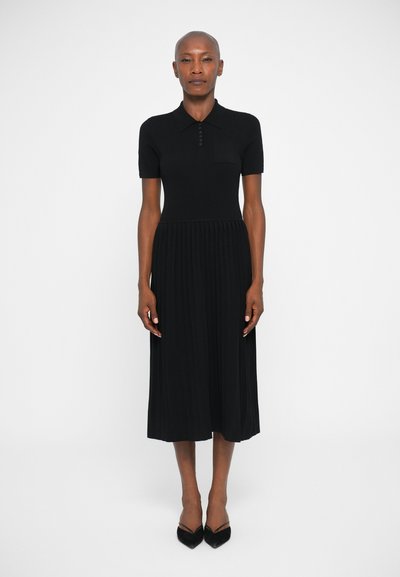 Black dress made of ribbed fabric, featuring a polo collar, short sleeves, a chest pocket, and a pleated skirt. Knee-length design.