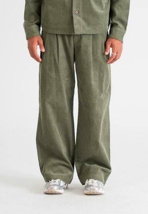 Corduroy outfit in olive green, featuring wide-leg pants with pleats and a button-up shirt. Textured fabric, relaxed fit, paired with gray shoes.