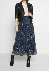 Mustat nahkatakki kevyen yläosan päällä, yhdistettynä vaaleansiniseen hameeseen, jossa on valkoinen kukkakuosi ja röyhelöhelma, käytetty mustien nilkkasaappaiden kanssa.