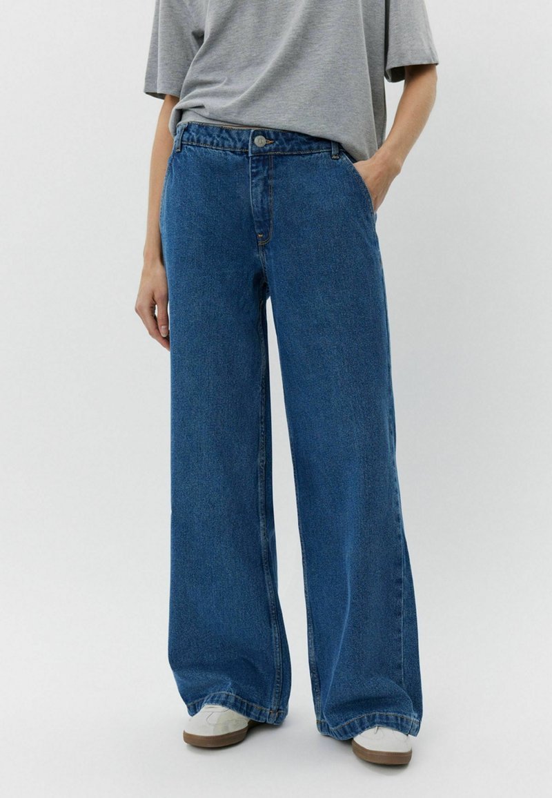 Jeans de denim azul de pierna ancha y cintura alta, con cierre de botón y bolsillos frontales. La tela presenta una textura suave con un color uniforme.