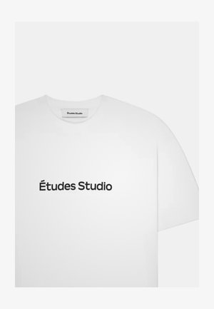 T-shirt blanc à manches courtes avec "Études Studio" imprimé en noir centré sur le devant et une étiquette portant le même texte à l'intérieur du col.