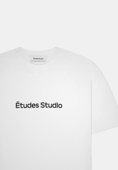 T-shirt blanc à manches courtes avec "Études Studio" imprimé en noir centré sur le devant et une étiquette portant le même texte à l'intérieur du col.