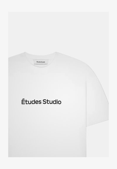T-shirt blanc à manches courtes avec "Études Studio" imprimé en noir centré sur le devant et une étiquette portant le même texte à l'intérieur du col.
