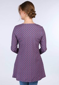 Lila Tunika mit einem sich wiederholenden Paisleymuster in Pink und Blau. Sie hat einen runden Halsausschnitt und Dreiviertelärmel sowie einen geraden Saum.