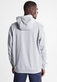Sudadera gris hecha de un tejido suave y texturizado. Presenta una capucha con cordón, mangas largas y puños acanalados con un ajuste relajado.