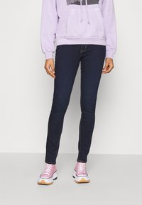 Jeans navy ajustados combinados con una sudadera ligera de color púrpura con un estampado gráfico. El calzado incluye zapatillas rosas con suelas blancas.