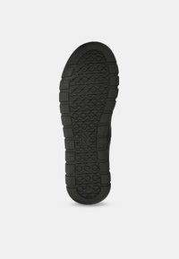 Suola di scarpa in gomma nera con un motivo texturizzato caratterizzato da lugs circolari e rettangolari per la trazione. Forma piatta e ampia per stabilità.