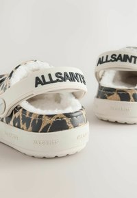 Mustat ja beiget liukuvat kengät pehmeällä sisäosalla, jossa on paksu valkoinen hihna, jossa lukee "ALLSAINTS", ja tekstuuriset kuviot materiaalissa.