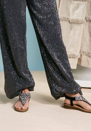 Pantaloni neri di paillettes con una superficie texturizzata, abbinati a sandali decorati con un design di foglia e una fascia nera.