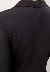 Indumento nero, aderente, con una texture liscia, con colletto classico e maniche lunghe, visto da dietro.