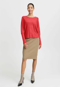 Röd långärmad topp i kombination med en beige ribbad midiklänning och svarta högklackade skor. Modellen bär mönstrade beige strumpor.
