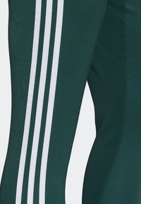 Zielone spodnie sportowe z trzema białymi paskami po bokach, wykonane z gładkiego, elastycznego materiału, zaprojektowane z myślą o dopasowanym kroju.