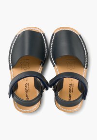 Granatowe skórzane sandały z białymi przeszyciami, z otwartym noskiem, paskiem na kostce i naturalną skórzaną wkładką. Posiadają wytłoczone logo marki na wkładce.