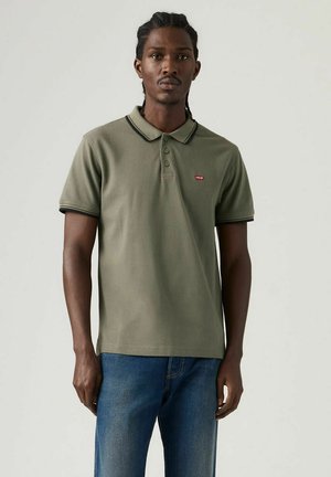 Olivengrøn polo med sort kant, tre-knaps lukning og lille rødt logo på brystet. Bomuldsmateriale med en glat tekstur.