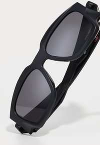 Las gafas de sol negras presentan un diseño audaz y angular con lentes oscuros, un acabado mate y un armazón ligero y flexible.