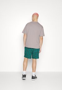 T-shirt gris à manches courtes associé à un short vert à motif zèbre noir, et des baskets noires avec des accents blancs. Vue de dos.