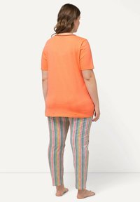 Camicia arancione a maniche corte abbinata a pantaloni slim-fit a righe multicolori su uno sfondo chiaro. Tessuto morbido.