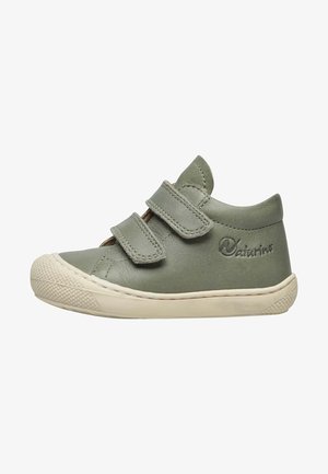 Chaussure en cuir verte avec deux bandes Velcro, bout arrondi, semelle en caoutchouc crème contrastante et capuchon de protection texturé. Marque sur le côté.