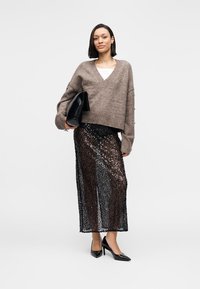 Καφέ πλεκτό πουλόβερ με λαιμόκοψη σε σχήμα V, κοντό μήκος, σε συνδυασμό με μαύρη μακριά φούστα με παγιέτες. Μαύρες ψηλοτάκουνες γόβες και μαύρο τσαντάκι χειρός ολοκληρώνουν το σύνολο.