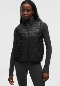 Musta toppaliivissä korkea kaulus, jossa tikattu rakenne ja vetoketjusuljenta. Päällä vastaava pitkähihainen paita, joka on istuvaa mallia.