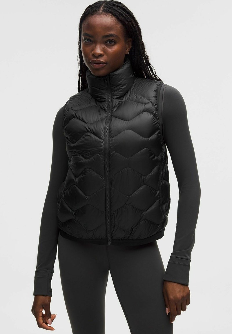 Musta toppaliivissä korkea kaulus, jossa tikattu rakenne ja vetoketjusuljenta. Päällä vastaava pitkähihainen paita, joka on istuvaa mallia.