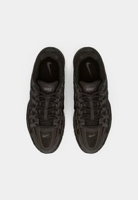 Mustat Nike-kengät, joissa on verkko- ja synteettinen päällinen, monimutkainen nauhoitusjärjestelmä ja teksturoitu pohja, jossa on näkyvä logo sivussa.