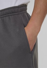 Pantalones de chándal grises con cintura elástica y bolsillos laterales. La tela parece suave con una textura lisa.