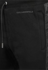 Sorte sweatpants med en struktureret sidelapel, justerbar snor i taljen og præget mærkning "KARL LAGERFELD" på forsiden.