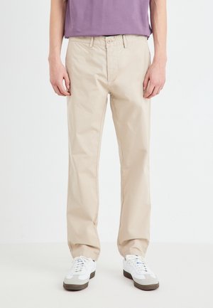 Chinos in cotone beige con design a gamba dritta; dotati di chiusura con bottone, passanti per la cintura e tasche; abbinati a sneakers bianche.