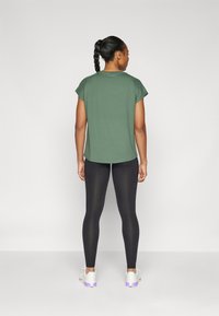 Top atletico verde a maniche corte con orlo arrotondato, abbinato a leggings neri aderenti e sneakers bianche con dettagli viola.