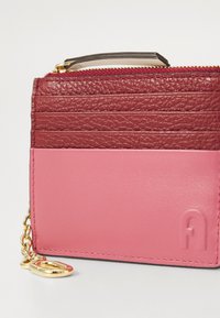 Portafoglio in pelle bicolore; parte superiore texturizzata color bordeaux con fondo rosa liscio; catena in metallo dorato; dettaglio logo impresso sul lato.