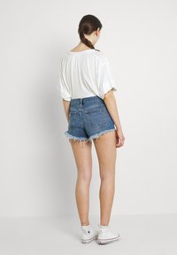 Džínové šortky s roztrhaným lemem, mají vysoký pas a modrou barvu. Slučují se s volným bílým tričkem a bílými vysokými teniskami.